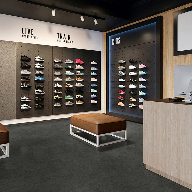 Sneaker store with shoe walls, benches and checkout area on recycled elastic flooring in a dark stone look with subtle mottled texture.