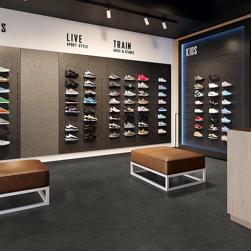 Sneaker store with shoe walls, benches and checkout area on recycled elastic flooring in a dark stone look with subtle mottled texture.