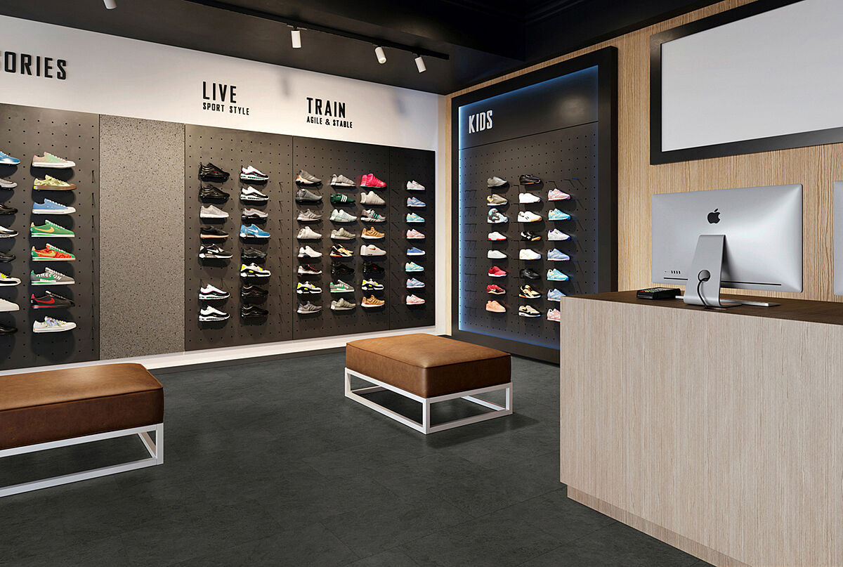 Sneaker store with shoe walls, benches and checkout area on recycled elastic flooring in a dark stone look with subtle mottled texture.