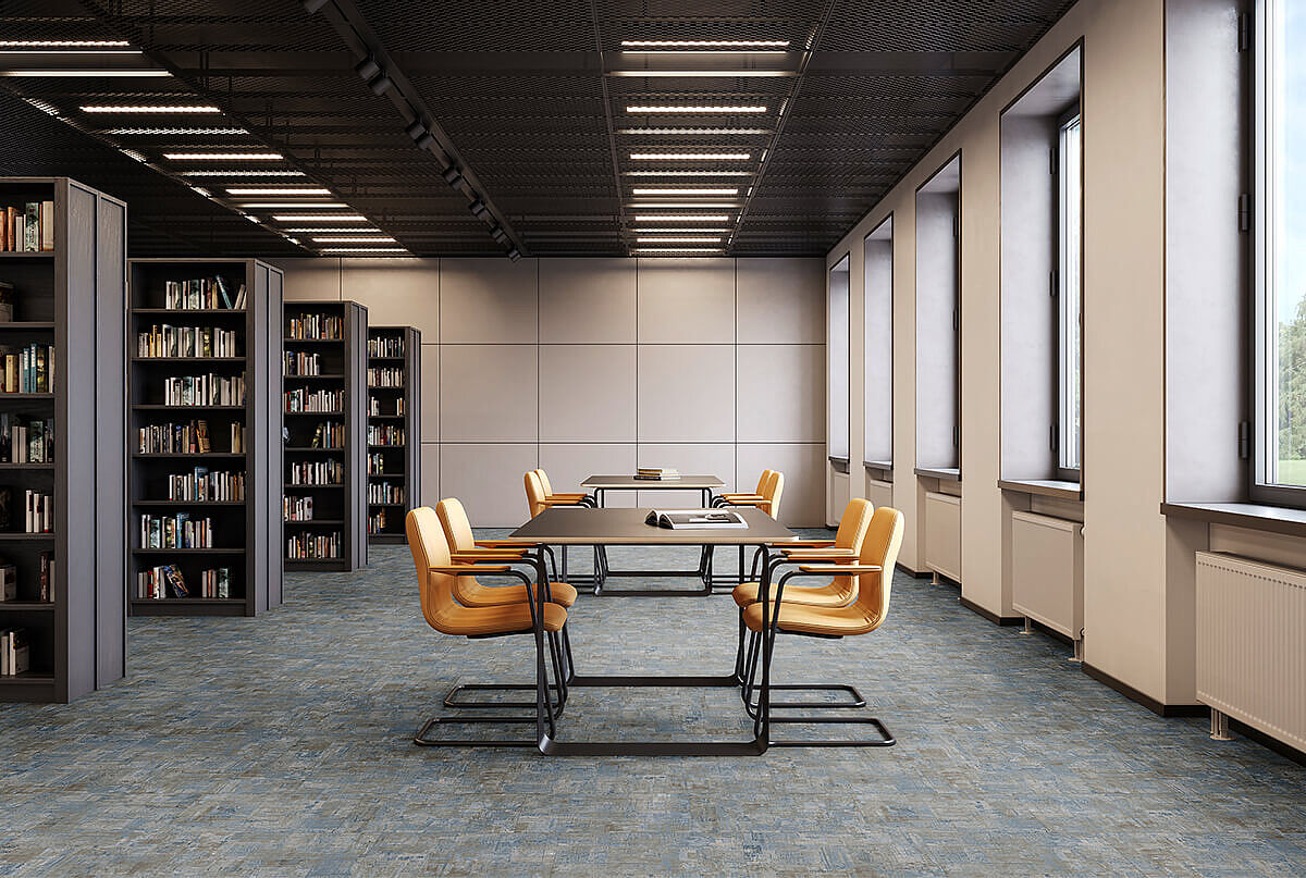 Reading room with bookshelves, tables and yellow chairs on recycled elastic flooring in a blue-grey mottled tile look.