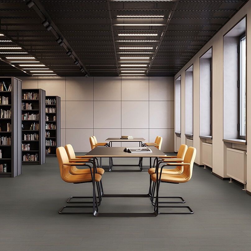 Library room with bookshelves, tables and yellow chairs on recycled elastic flooring with a modern dark grey texture.